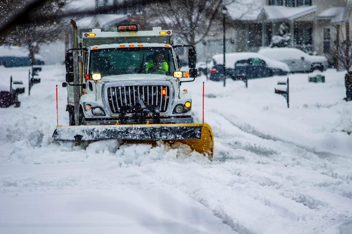 Snowplow service truck clearing residential roads of snow while flakes are still falling
