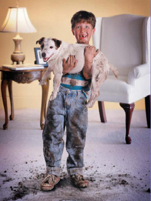 Child holding a dog and standing on a muddy carpet