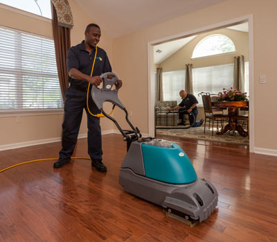 A ServiceMaster technician cleaning a wood floor using specialty equipment