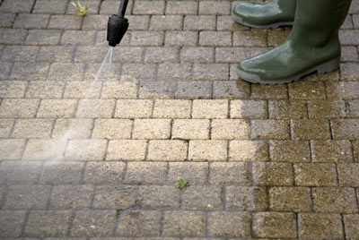 A person in boots using a pressure washer to clean concrete