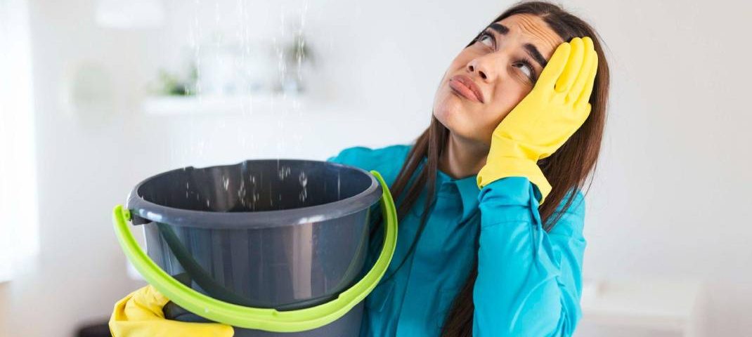 A young woman holding bucket in her hand for water leaking from top roof