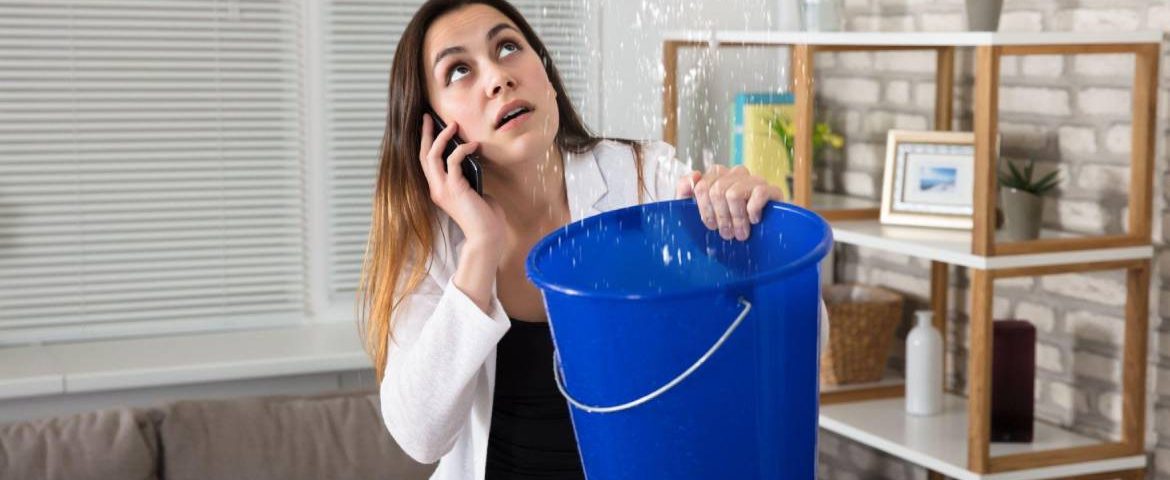 A young woman holding bucket in her hand for water leaking from top roof and call for help to the restoration company