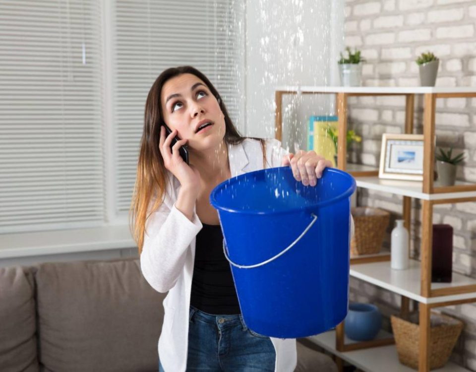 A young woman holding bucket in her hand for water leaking from top roof and call for help to the restoration company